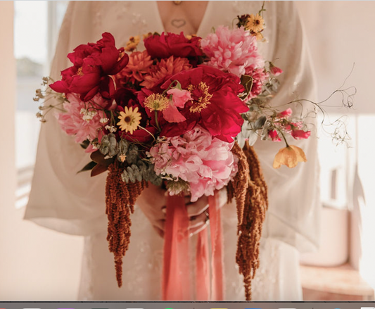 A bright wedding bouquet of red, pink and orange flowers being held by a bride