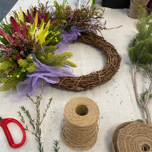 A festive wreath is being made on a table, with bright australian native flowers in red, gold and green.